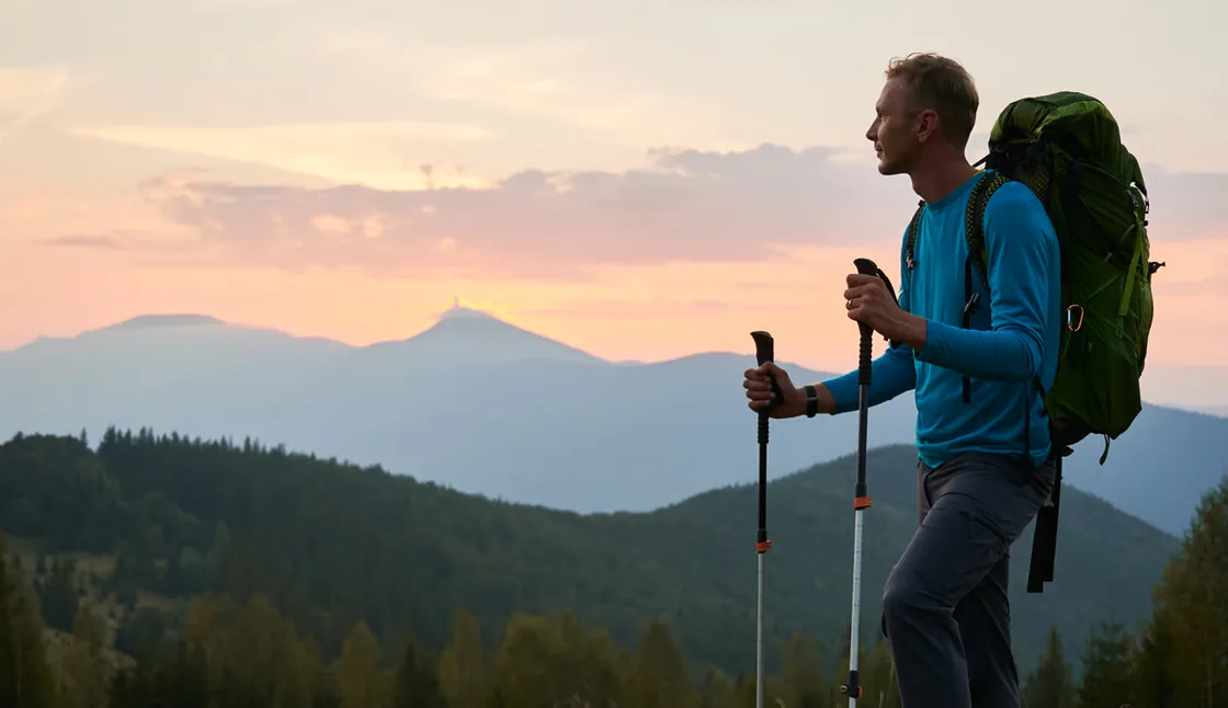 Uitgeruste wandelaar op een heuveltop tegenover blauwige bergkammen bij zonsondergang