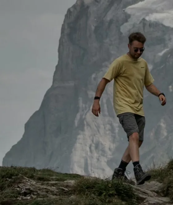 Wandelaar in geel T-shirt daalt een grasrug af tegenover een hoge rotswand