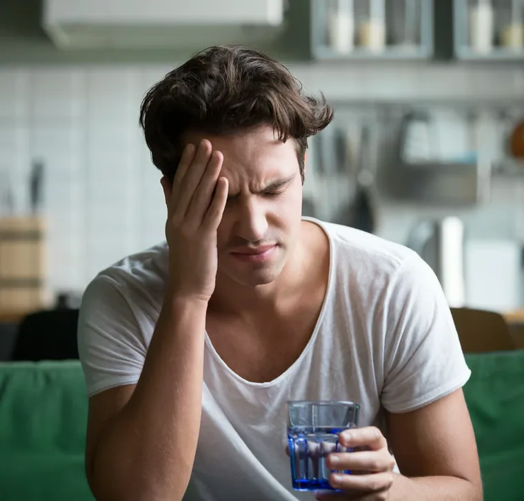Man zit in zijn keuken met de hand tegen zijn slaap, getekend door vermoeidheid