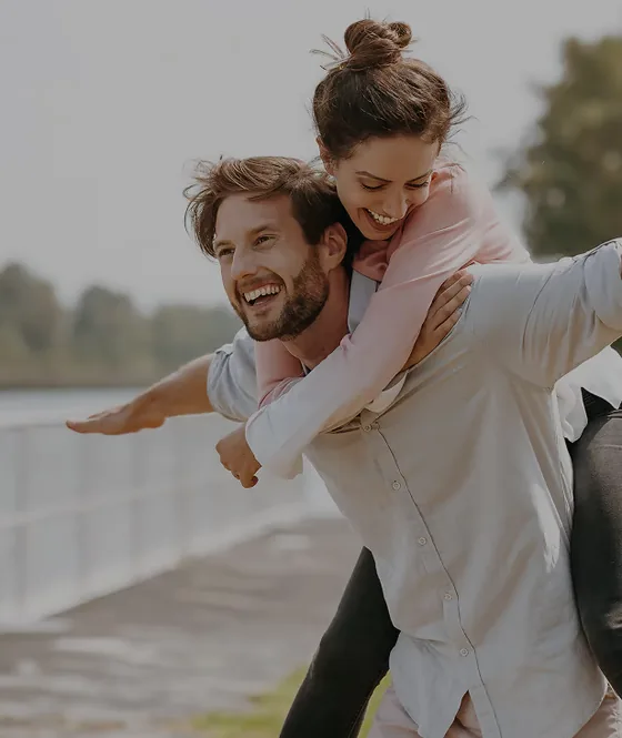 Man draagt lachend een vrouw op zijn rug langs een wandelpad aan een meer